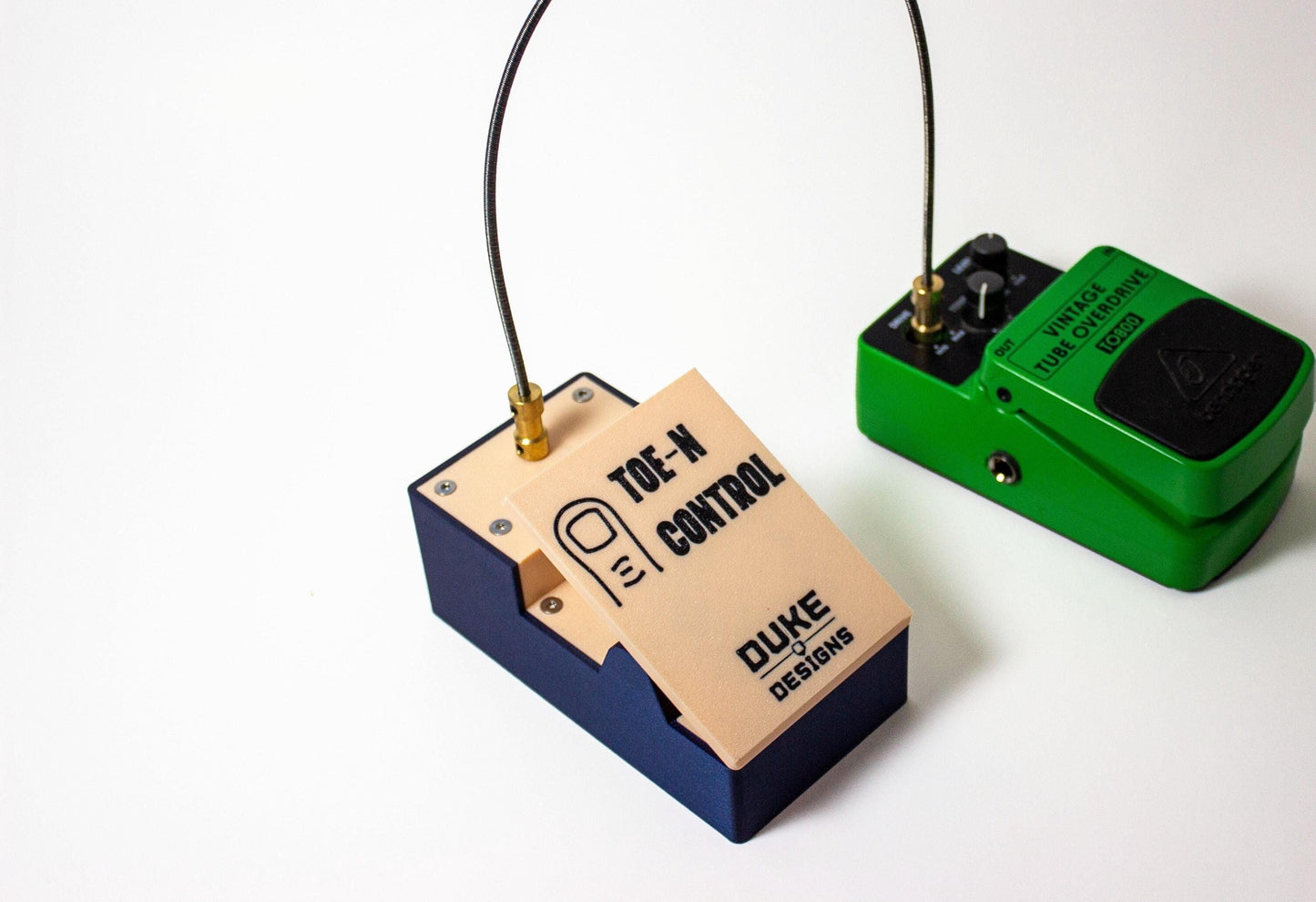 A small expression guitar pedal connected to another guitar pedal knob using a flexible shaft. The words Toe-N Control and Duke Design are present on the pedal